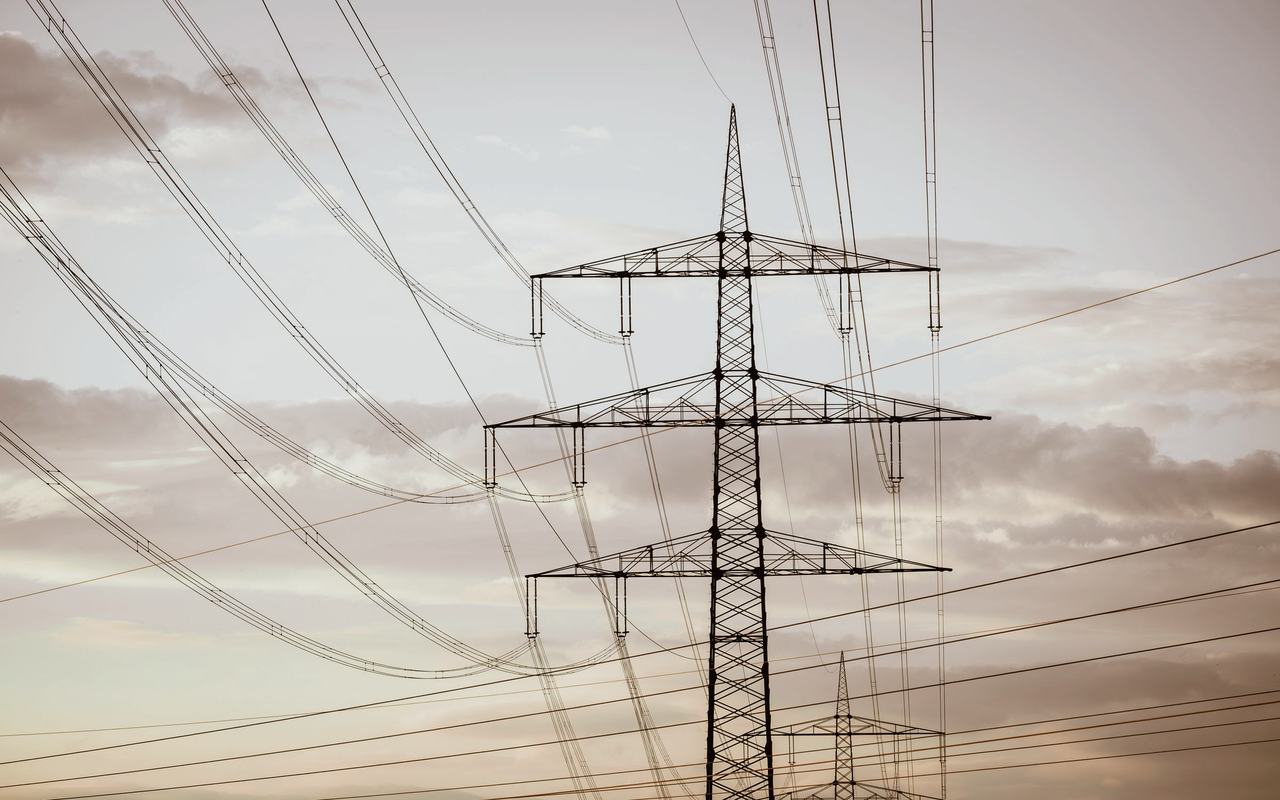 Silhouetted electricity pylons and power lines against a dramatic sky at sunset.