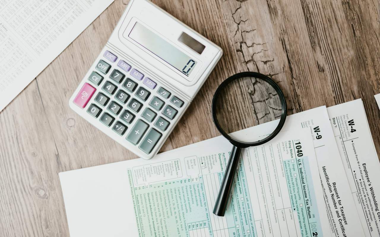 Tax forms laid out with a calculator and magnifying glass on a wooden surface, perfect for finance themes.