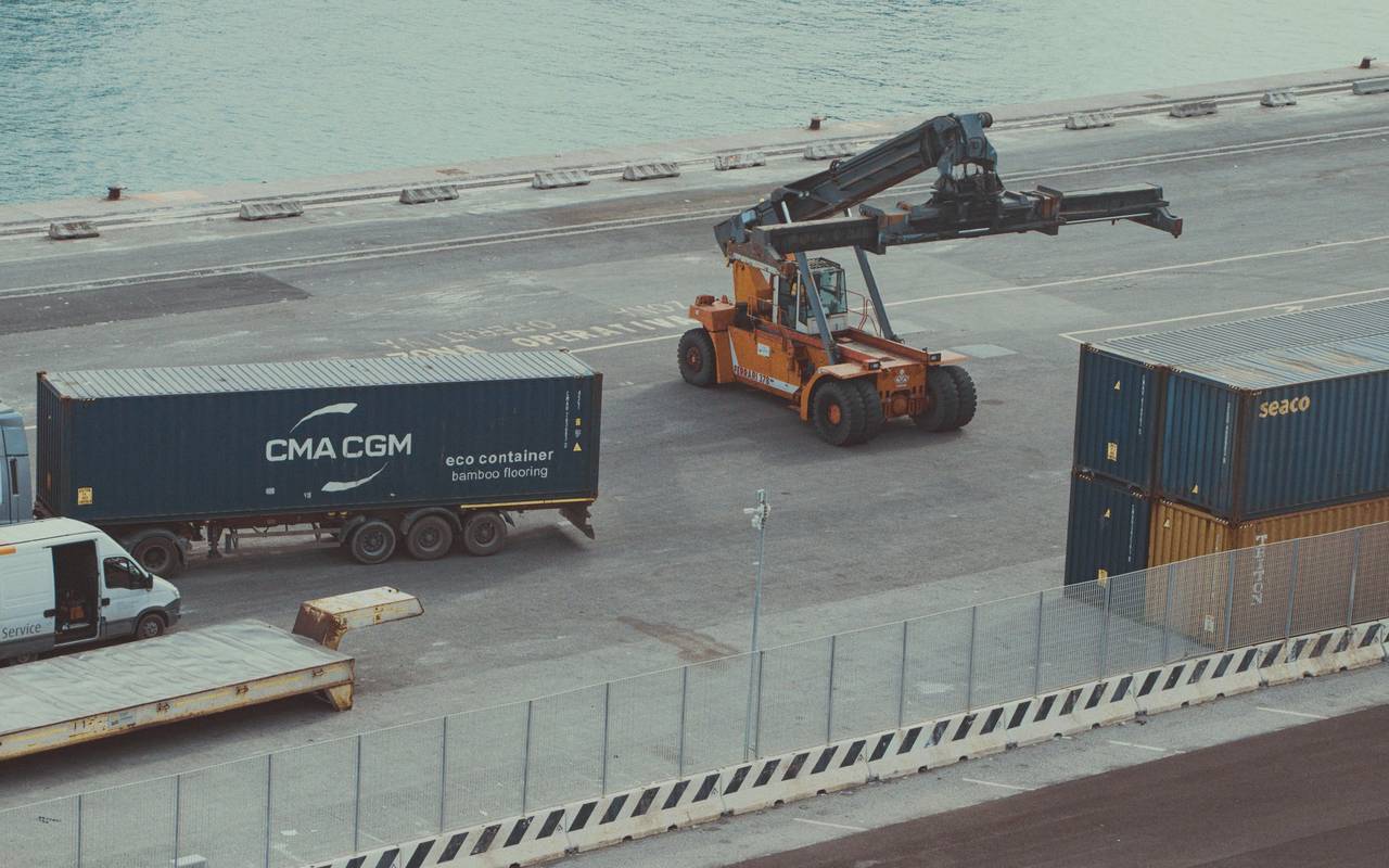 View of a busy container terminal with trucks and forklifts managing cargo under daylight.
