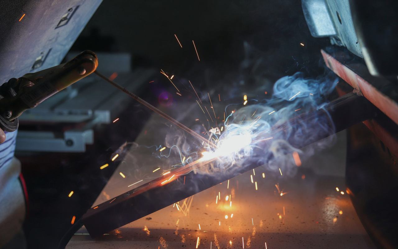 Close-up of a welder at work with sparks and smoke in an industrial setting.