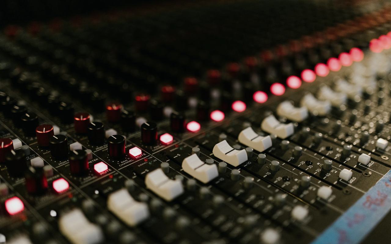 Close-up of a sound mixing console with illuminated control knobs in a music studio.